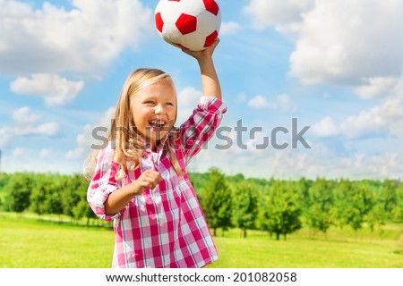 Cute little blond girl in pink shirt throwing soccer ball laughing
