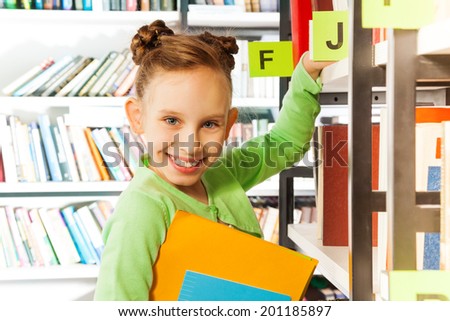 Smiling girl searching books in library