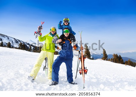 Mom, dad with child on his shoulders in ski masks holding ski on mountains background