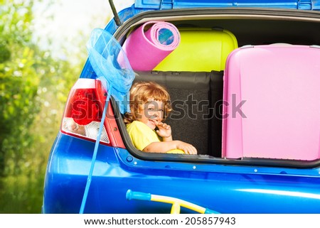 Little three years old boy sitting in the car trunk waiting for parents to put bags for the trip in the car