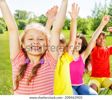 Four children sitting in row with hands up