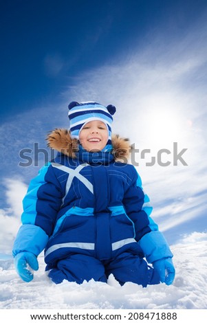 Happy 5 years old Caucasian boy sitting in snow outside in winter