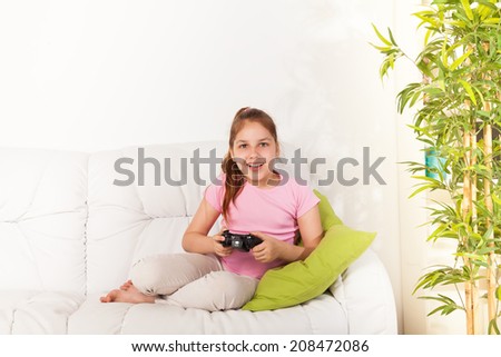 Happy Caucasian girl playing video games holding game controller sitting on the coach in living room