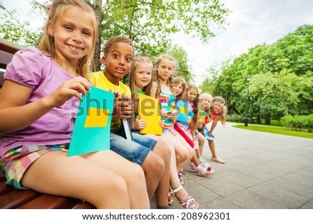 Funny children sit close on bench with books