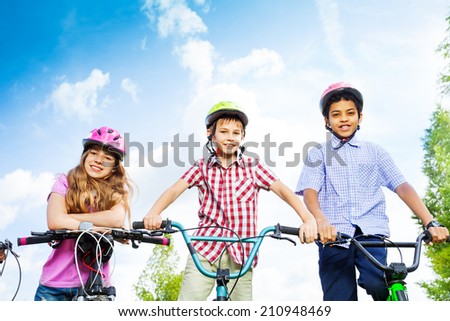 Three kids in helmets hold bike handle-bars