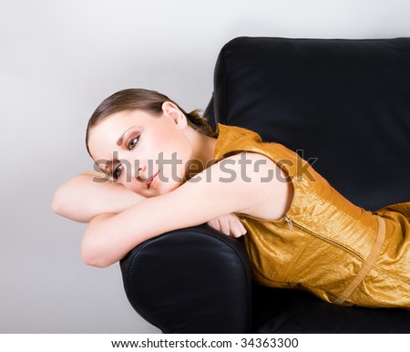 Young woman in gold dress sleep on black leather sofa