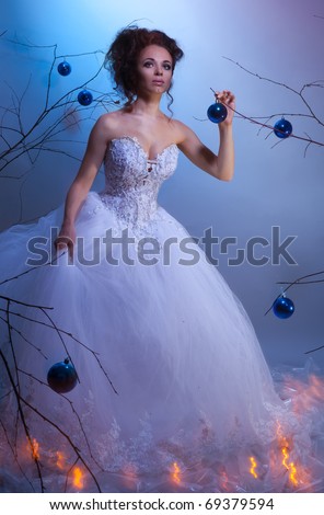 Bride in a wedding dress walking between winter trees decorated with Christmas balls, shoot with both continuous and instant flash light made with professional makeup artist and hairdresser