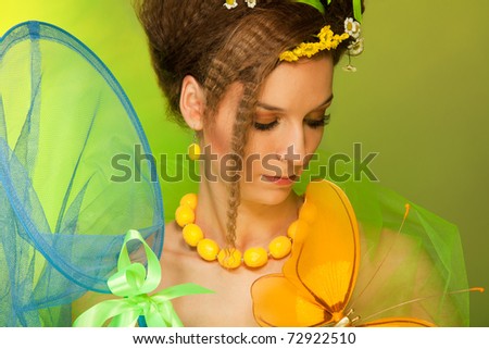 Summer girl catching butterfly with butterfly net - beauty portrait of attractive woman with bows and flowers in her hair and dress, with professional hairstyle and make up