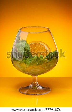 Glass with mint and orange drink on yellow background