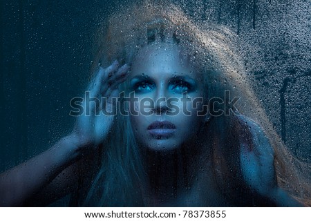 Beautiful woman looking through night window with rain outside