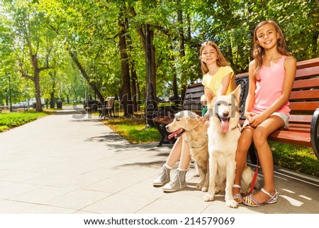 Two girls with dogs sitting in park on bench