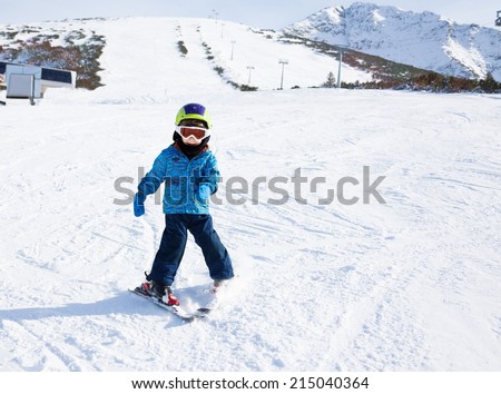 Boy in ski mask learns skiing on snow downhill of the mountain