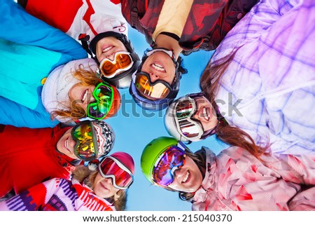Seven happy smiling friends standing in circle wearing ski mask on the skies background