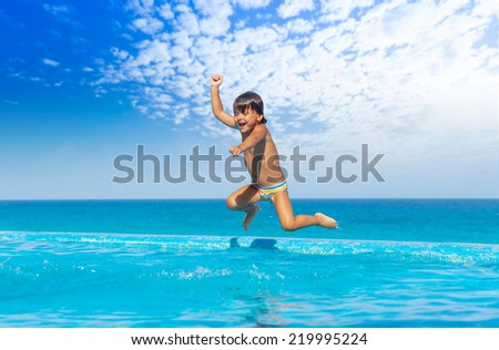 Boy jumps in swimming pool with seaside background