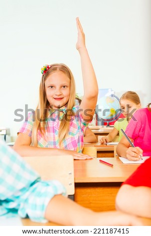Blond girl holds hand up in class and smiles