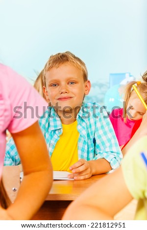 Blond boy looks straight and sit with other pupils