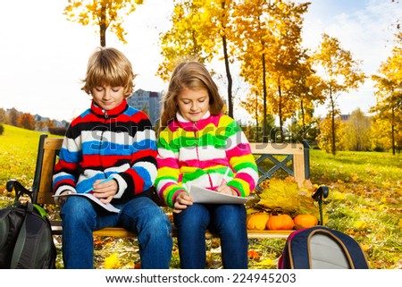 Portrait of two happy blond kids, twins brother and sister sitting on the bench after school drawing pictures on paper