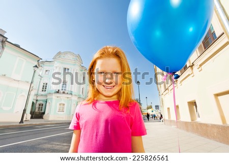 Smiling girl with flying balloon stands on street