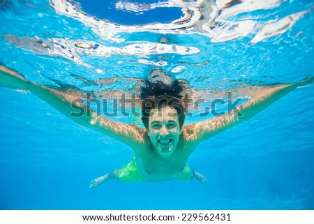 Smiling man swims under the crystal-clear water