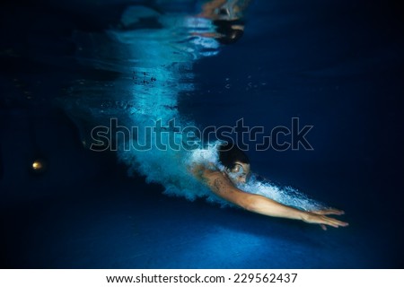 Man with splash swimming under dark blue water