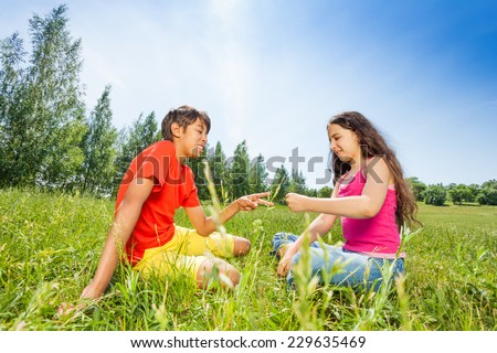 Two children play rock-paper-scissors on grass in summer
