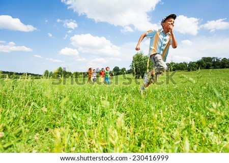 Excited boy runs away from his mates in field during summer time
