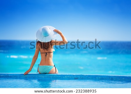 Woman from back with white hat  sits on coast