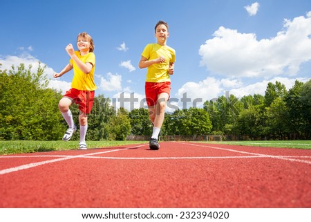 Two boys run while competing who is faster on stadium road in summer