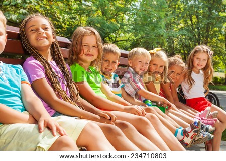 Close group portrait of happy little diverse looking boys and girls sitting on the bench in the nice park