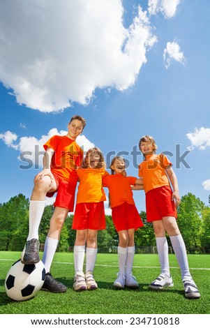 Laughing children of different height with football standing in a row on football field