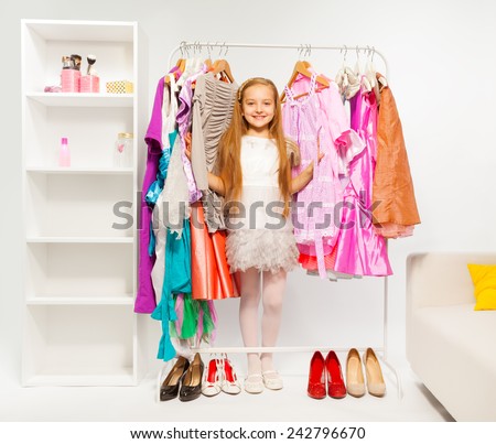 Cute girl among colorful bright dresses, clothes