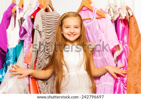 Smiling girl stands among dresses on hangers
