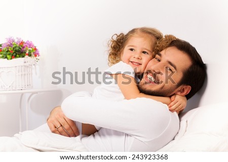 Smiling father and daughter hug on the white bed