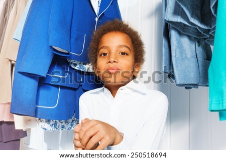 Cute African boy in white shirt sits under hangers