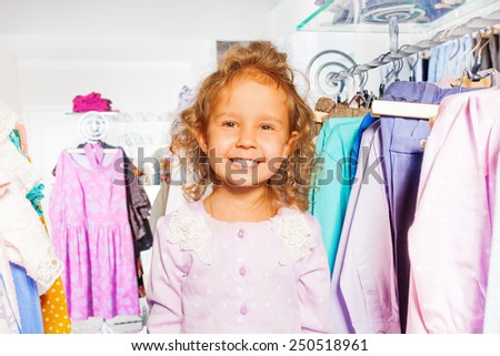Cute girl among clothes on the hanger in  shop