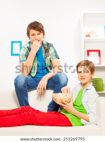 Happy boys eat popcorn while sitting on white sofa