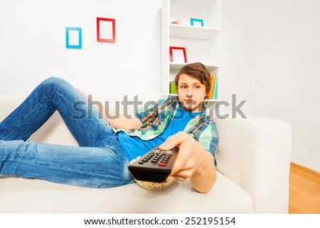 Boy switches remote control laying on white sofa