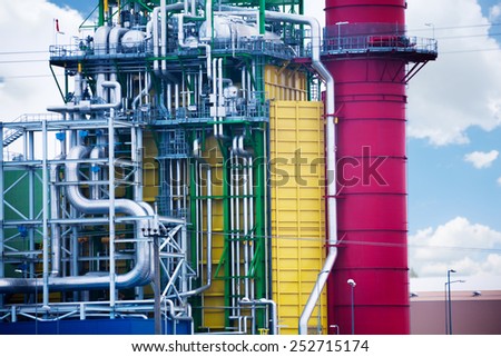 Detailed close up view of factory plant with colorful tower and metallic tubes on sky background