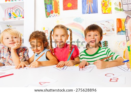 Group of diverse looking children in kindergarten class drawing letters in early reading class