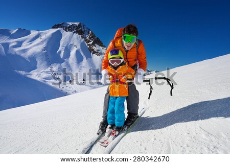 Little boy learns to ski on mountain resort with instructor helping to learn how to turn with mountain on background