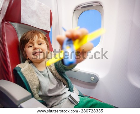 Happy little 4 years old boy play with plastic aircraft sitting in chair in salon of jet  going on vacation