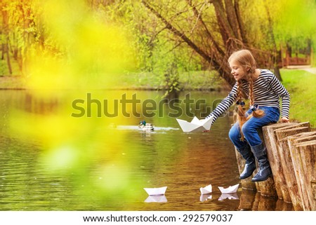 Girl sitting near pond playing with paper boats
