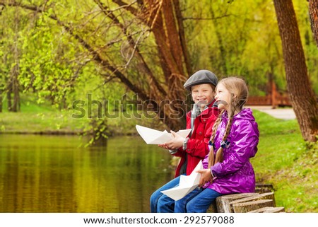 Smiling girl and boy sit near nice pond playing