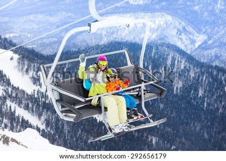 Happy family with mother and little boy sitting on ski lift waving hand with mountains and forest on background