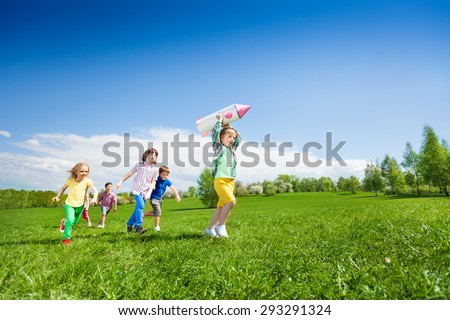 Children run after boy holding rocket carton toy