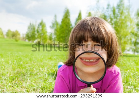 Funny boy smiles through magnifier, lays on grass