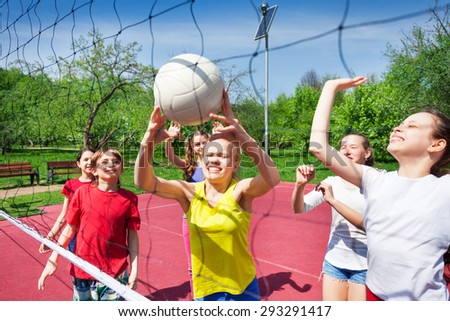 Excited teens play near volleyball net on court