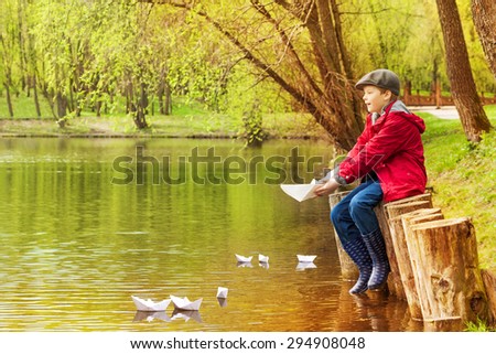 Boy alone near pond playing with  paper boats