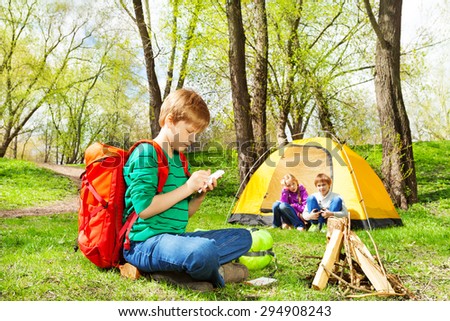 Boy with red backpack writes notebook at camping