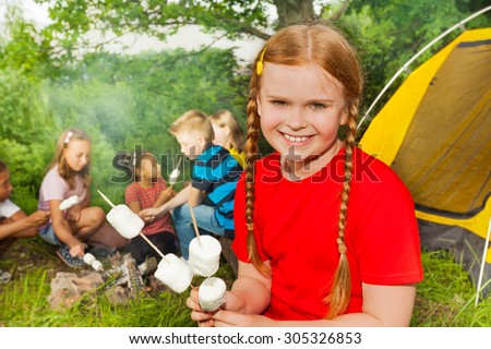 Smiling girl camping and holding  marshmallows